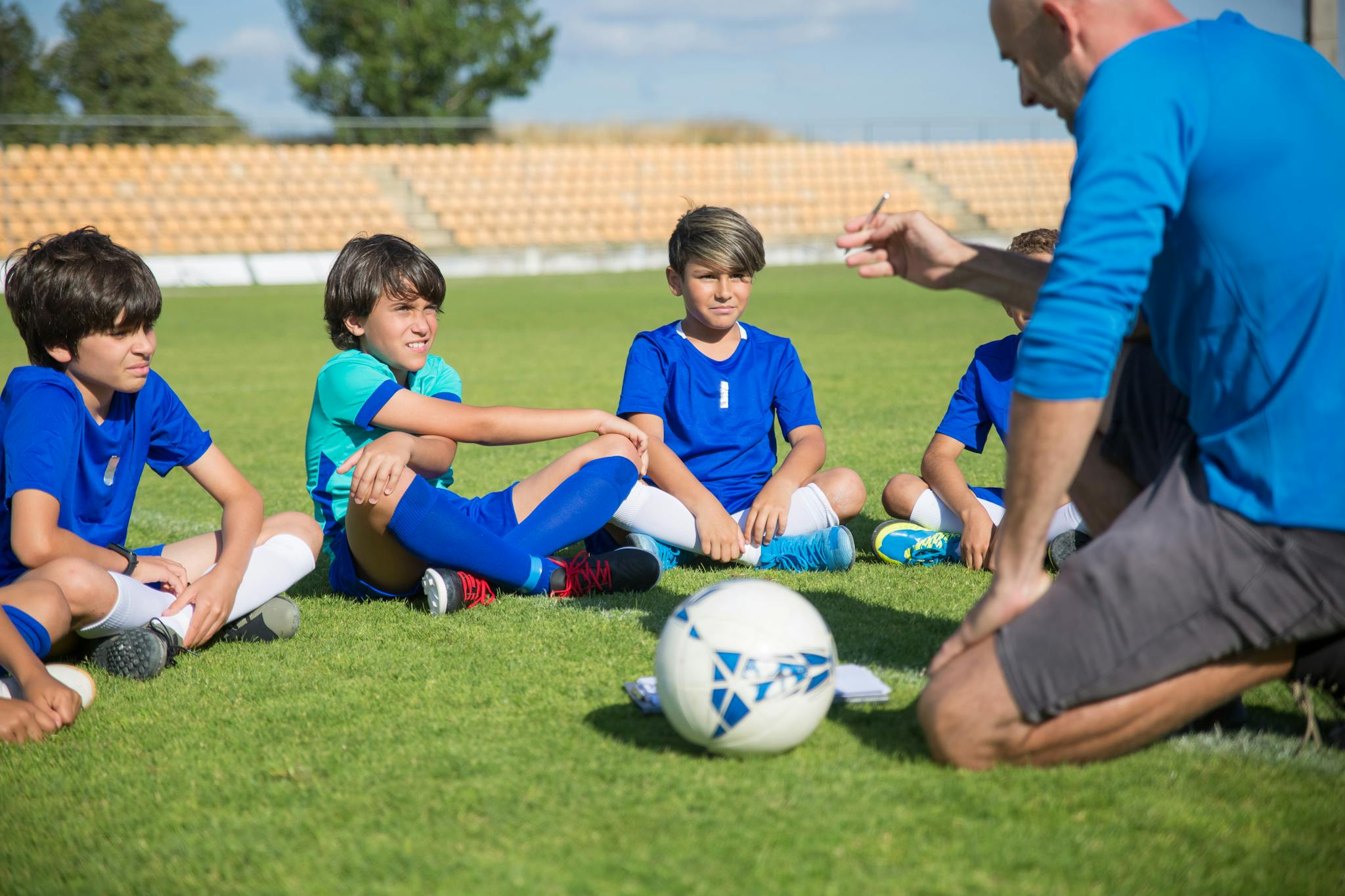Boys listen intently to their soccer coach on a sunny soccer field.